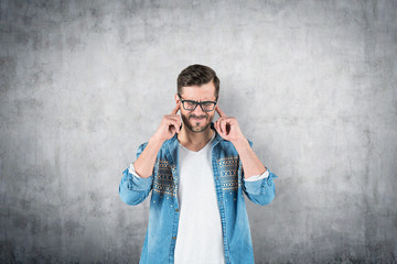 Man in glasses covering his ears, concrete