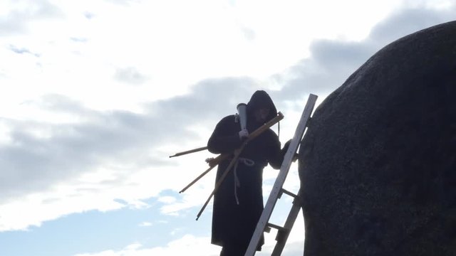man in ancient hoodie with telescope climbing to rock top silhouette