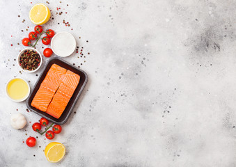 Plastic container with fresh salmon slice with oil tomatoes and lemon on stone kitchen background. Space for text