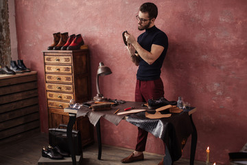Fototapeta na wymiar gorgeous pleasant bootmaker holding a shoe at shoemaker's shop. full length photo