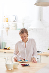 happy young woman preparing tasty snacks at the kitchen table in the morning light