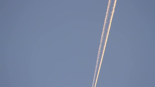Avi&oacute;n en el cielo cruzando en diagonal la pantalla y dejando rastro o estela con reflejo de sol de atardecer
