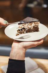 Delicious chocolate cake in white plate in hand on cafe background, closeup. selective focus, noise effect