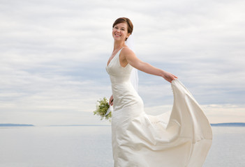 Beautiful, happy, smiling bride in white satin wedding gown dancing on a beach