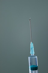 The end of the syringe with a needle filled with liquid, on a neutral background.