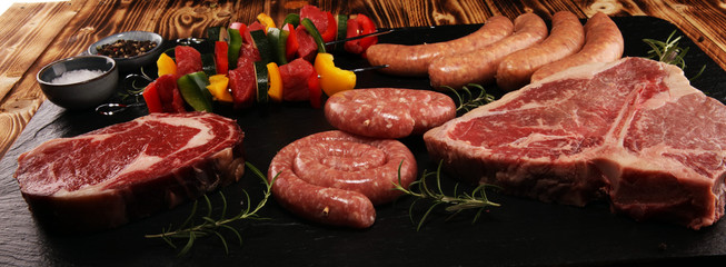 Assorted delicious raw meat with vegetable on a barbecue with t-bone steak, sausages and meat...