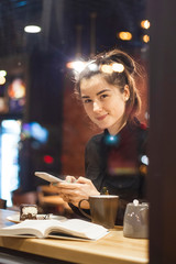 An attractive girl sits in front of a panoramic window at the cafe, drinking coffee and eating dessert. selective focus, noise effect