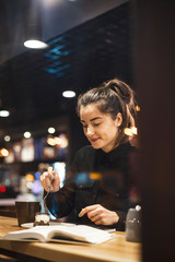 An attractive girl sits in front of a panoramic window at the cafe, drinking coffee and eating dessert. selective focus, noise effect