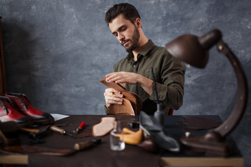 young awesome craftsman working with different kinds of leather. man is going to sew insoles