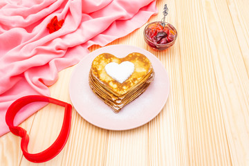 Heart shaped pancakes for romantic breakfast with strawberry jam and heart form. Shrovetide (carnival) concept. On wooden background with pink linen cloth