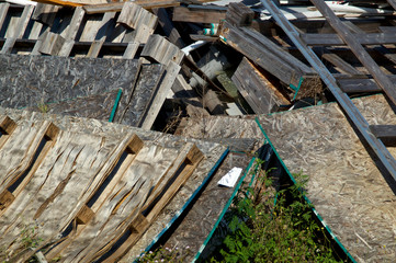 A heap of wooden pallets or skids and sheets of particle boards in a pile outdoors in sunlight.