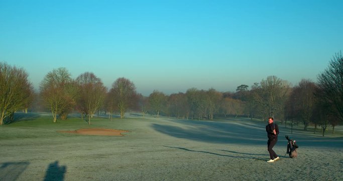 A golfer chips a shot on a winters morning golf course in slow motion.