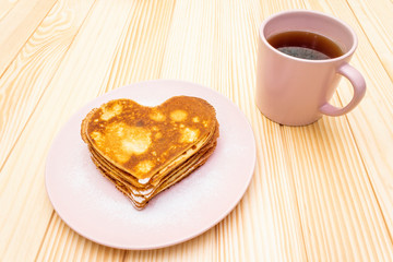 Heart shaped pancakes for romantic breakfast with strawberry jam and black tea. Shrovetide (carnival) concept. On wooden background