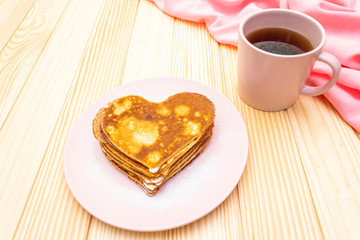 Heart shaped pancakes for romantic breakfast with strawberry jam and black tea. Shrovetide (carnival) concept. On wooden background