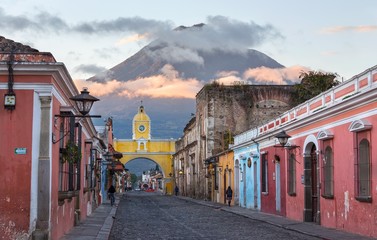 Colonial Architecture and Street Scene during Early Morning Sunrise in Antigua Guatemala with Santa Catalina Arch and Agua Volcano in the Background - obrazy, fototapety, plakaty