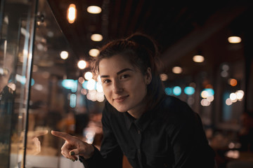 Gorgeous smiling young woman with dark hair eating cake and drinking coffee at a cafeteria in the evening sitting by the window. selective focus, noise effect