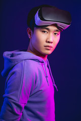 Half-size studio portrait of Asian cyberspace player with his vr glasses taken off , mounted on head, looking at camera isolated in casual clothes in dark blue background with copyspace