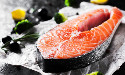 fresh raw salmon steak with broccoli, lemon, olive, pepper and aromatic herbs on the dark background
