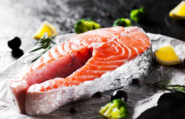 fresh raw salmon steak with broccoli, lemon, olive, pepper and aromatic herbs on the dark background
