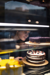 smiling mature female staff offering fresh pastry in sweet-shop. selective focus, noise effect