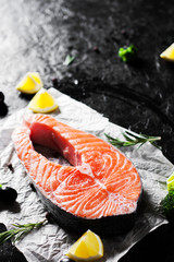 fresh raw salmon steak with broccoli, lemon, olive, pepper and aromatic herbs on the dark background
