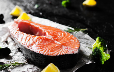fresh raw salmon steak with broccoli, lemon, olive, pepper and aromatic herbs on the dark background