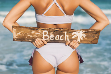Sexy woman wearing swimsuit with old wooden sign on the beach