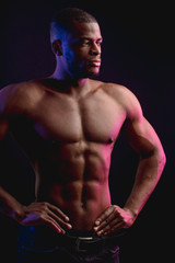 Fototapeta na wymiar African male athlete with naked torso with six pack posing against dark wall. Low key photo.
