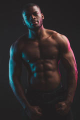 Fototapeta na wymiar African male athlete with naked torso with six pack posing against dark wall. Low key photo.