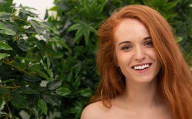 Fototapeta premium Cheerful redhead woman laughing through monstera leaves