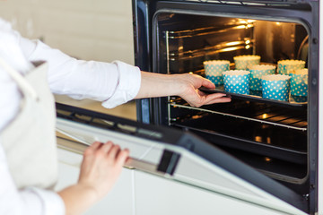 woman's hands putting the baking sheet with cupcakes in the oven, close up cropped photo