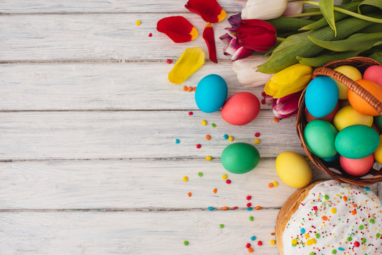 Colorful easter eggs,cake,spring tulips  on wooden texture background.On a white wood table,colored eggs,flowers,bread.Happy religious day,traditional for people. Top view.Copy space.