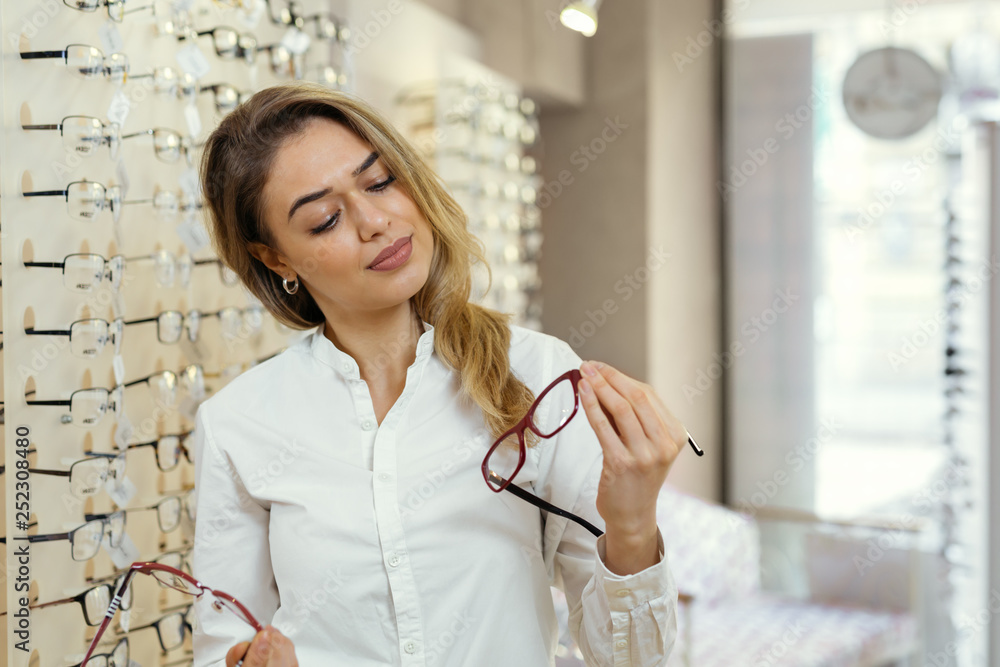 Wall mural choosing the right on. woman buying glasses in optic store