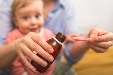 close up of mother pouring cough syrup. blurred baby boy in background