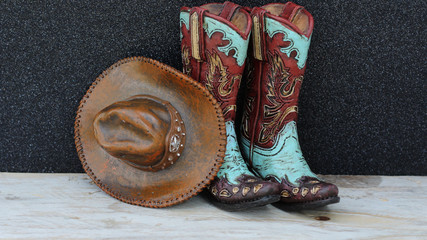 Pair of cowboy boots and hat standing on wood with a black background with writing space