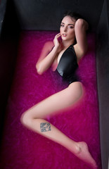Fototapeta na wymiar beautiful girl in a black bath with pink water and brilliance