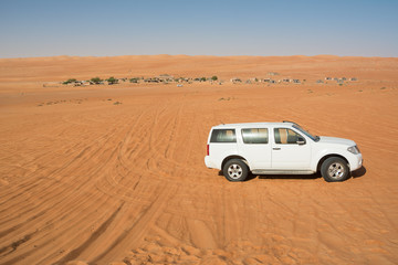 Fototapeta na wymiar Off-road vehicle in the Wahiba Sand Desert and Bedouin camp in the background (Oman)