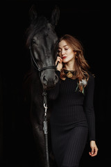 Obraz na płótnie Canvas Portrait of young pretty woman and black horse on black background isolated. Fashion concept