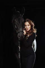 Fototapeta na wymiar Portrait of young pretty woman and black horse on black background isolated. Fashion concept