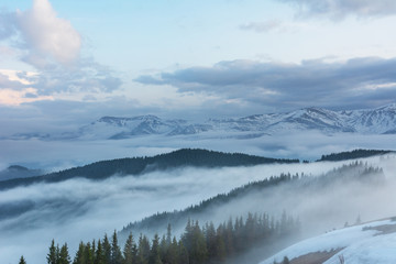 Fototapeta na wymiar Magic spring fogs in Ukrainian Carpathians overlooking the snow-capped mountain peaks from the picturesque mountain valley with tourists in tents.