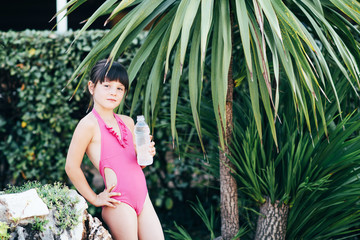 Cute cute girl in a pink swimsuit with a bottle of water in her hands spending time in the nature in the summer