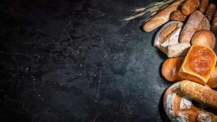 Fototapeten Auswahl an frisch gebackenem Brot auf dunklem Hintergrund. Weiß- und Roggenbrot, Brötchen mit Kopierplatz © Andrii