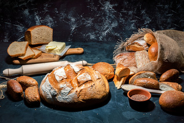 Différents types de pain et petits pains sur fond sombre. Assortiment de pains frais, viennoiseries, viennoiseries, pain blanc et pain de seigle