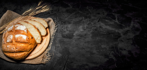 Round loaf bread with some slices cut on dark background with copy place
