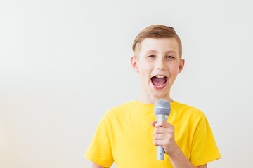 Emotional boy sings a song into the microphone with his mouth wide open. Copy space