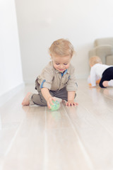 Cute infant baby boy crawling on the floor at home and playing with colorful ball