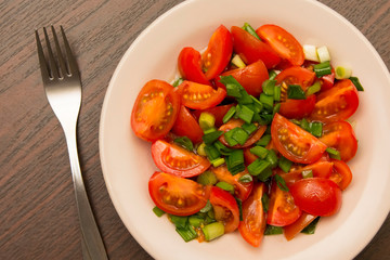 metal fork and small cherry tomatoes in a plate on a brown table