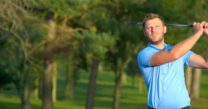 A Golfer hits a ball out of a sand trap in slow motion, the ball falling back into the frame.