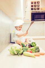 Baby boy sitting among vegetables in the kitchen and prepares for cooking