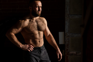 Fototapeta na wymiar Portrait of topless bearded caucasian Athletic Male Fitness Model posing near dark wall background